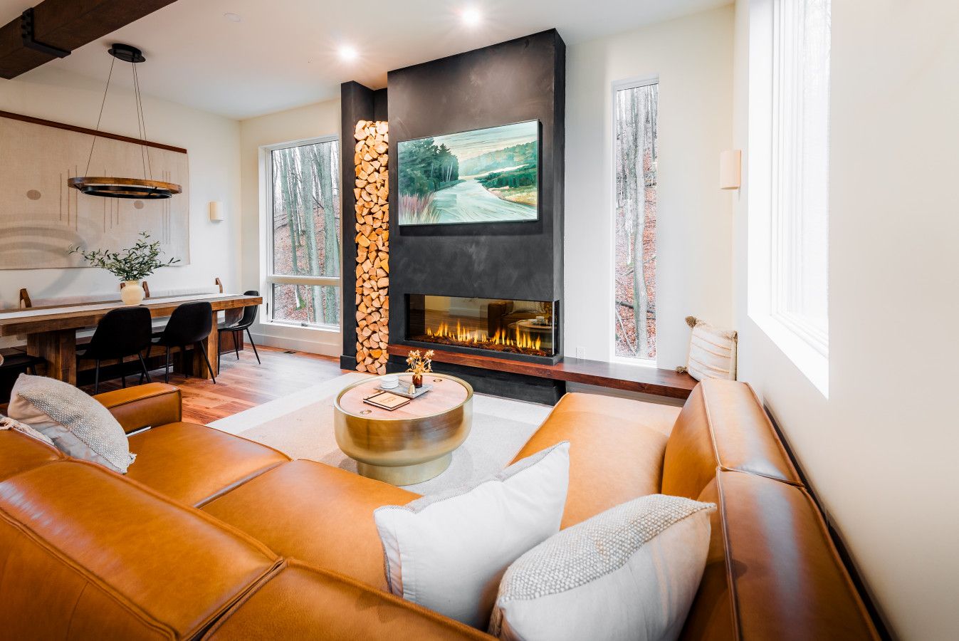 A modern living room with a fireplace, leather sofas, a dining area, and large windows.