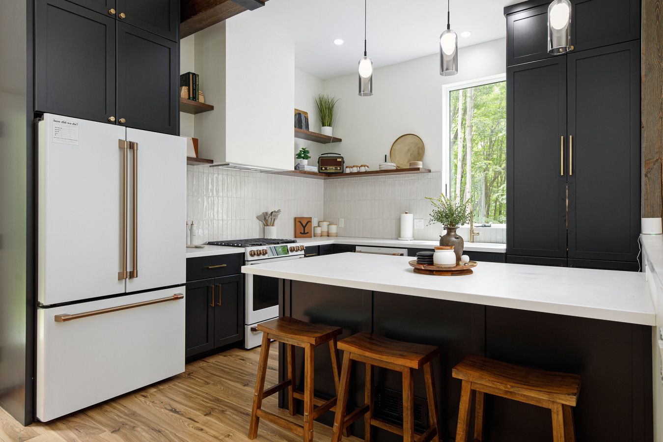 A modern kitchen with dark cabinetry, a white island with stools, and pendant lighting.