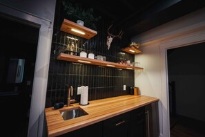 Une cuisine moderne avec des plans de travail en bois, un crédence en carreaux noirs et des étagères remplies d’ustensiles de cuisine.