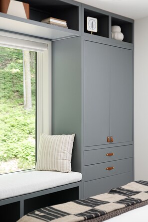Une pièce avec une banquette intégrée près d’une fenêtre, une armoire grise avec des poignées en cuir et un tapis à motifs.