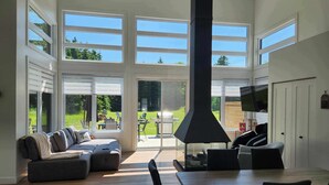 A spacious living room with a large fireplace, a dining area, and a view of the backyard through large windows. - Ô 7e ciel spa and massage (weedon)