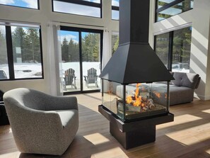 A modern living room with a glass fireplace, large windows, and a cozy seating area. - Ô 7e ciel spa and massage (weedon)