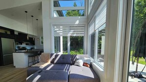 A modern living room with a sectional sofa, large windows, and a kitchen area. - Ô 7e ciel spa and massage (weedon)