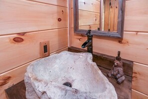 Un baño de cabaña de madera con un lavabo de piedra, un espejo y una pequeña estatua.
