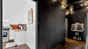 Een moderne keuken met witte kastjes, een houten aanrecht en een spatwand. Rechts is een zwarte muur met een spiegel en verlichting.