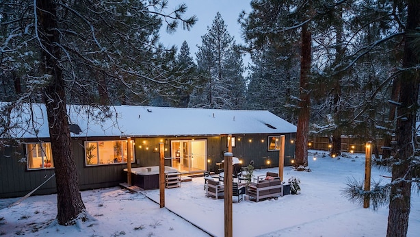 Una cabana amb un bany d'hidromassatge, seients a l'exterior i llums penjants en un bosc nevado.