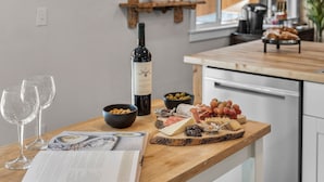 Taula de fusta amb una ampolla de vi, gots, un bol d'olives, formatge i raïm.