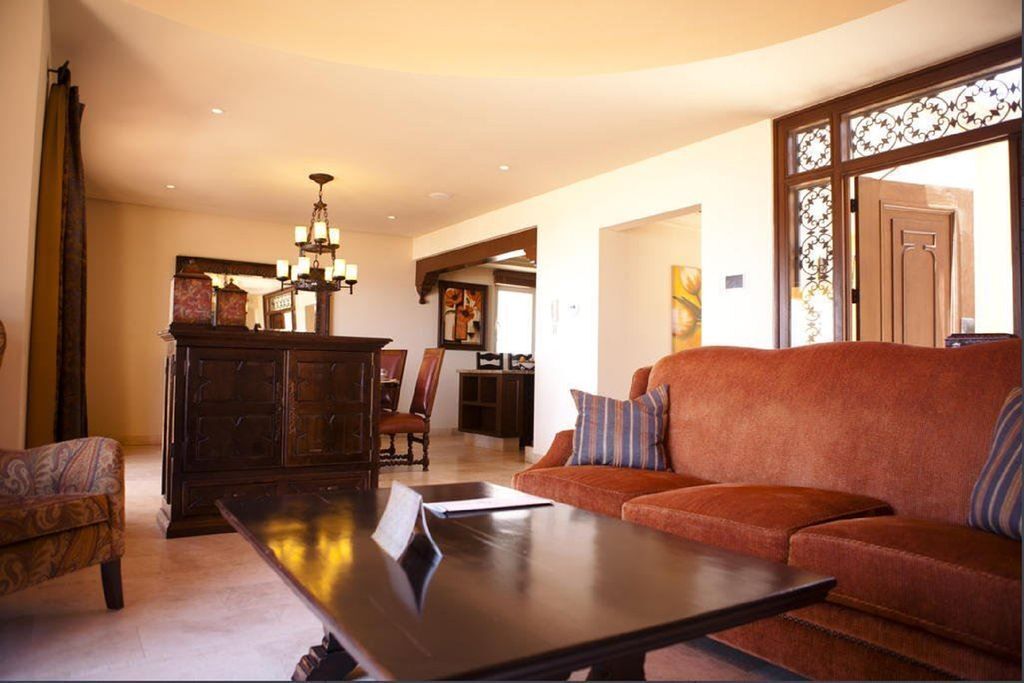 A spacious living room with a dark wooden coffee table, a red sofa with striped cushions, and a traditional wooden cabinet.