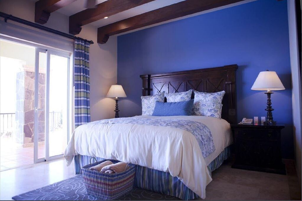 A bedroom with a large bed, two bedside lamps, a nightstand, and a view of a balcony.