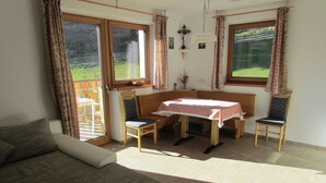 A room with a bed, a table with chairs, and large windows with curtains.