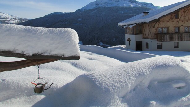 A snow-covered mountain landscape with a wooden building featuring a balcony and a wooden fence.