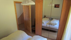 A bedroom with a bed, a wooden wardrobe, and a mirror reflecting the bed.