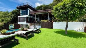 Una casa moderna de dos pisos con piscina, mobiliario exterior y un porche cubierto.