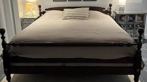 A large bed with a wooden frame, a ceiling fan, and three framed pictures on the wall.