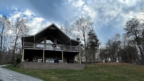 A large, two-story building with a balcony on the second floor, surrounded by trees and a clear sky.