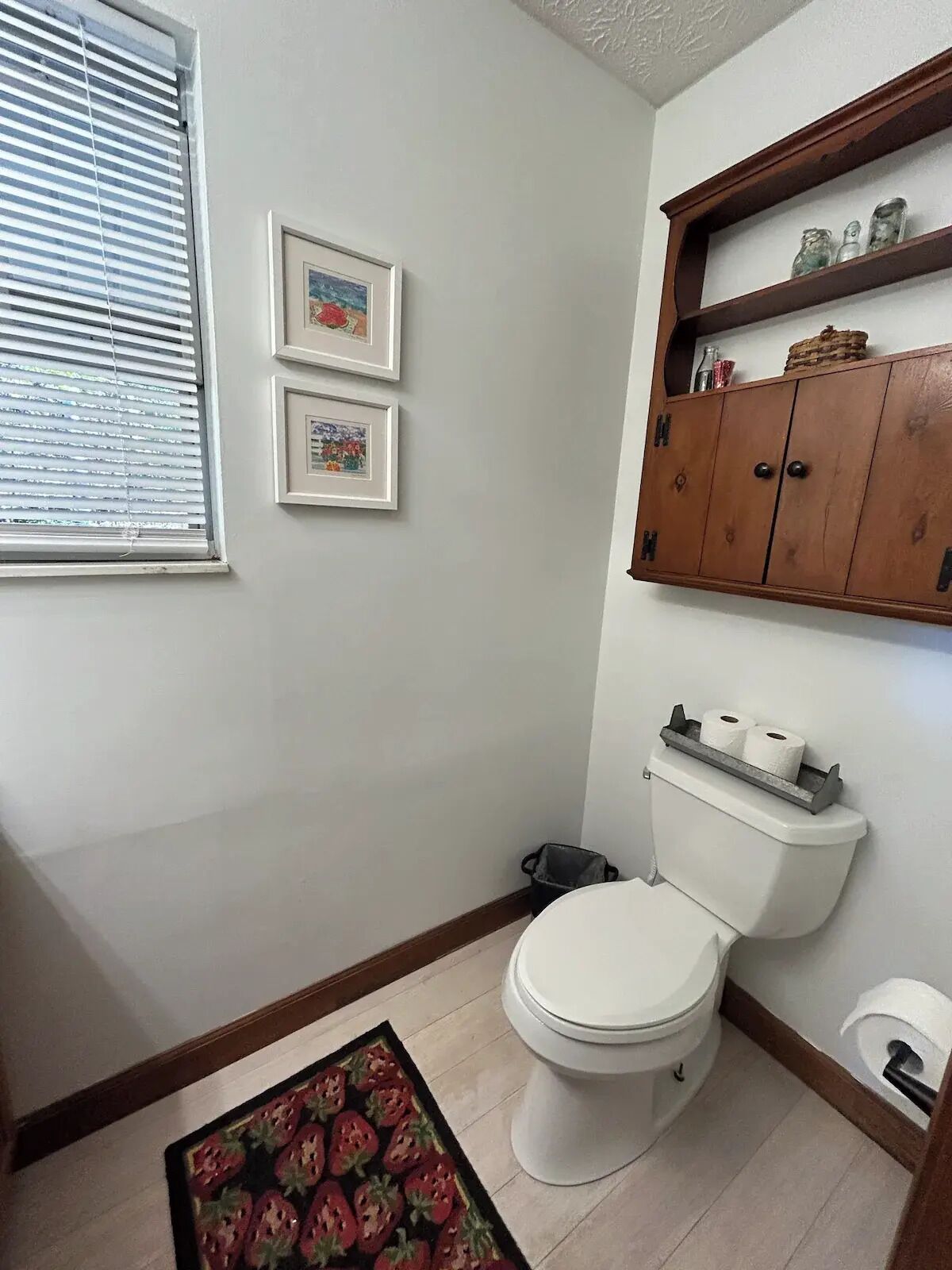 Ein Badezimmer mit Toilette, einem gerahmten Bild an der Wand und einem Regal über der Toilette.