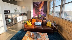 Una sala de estar moderna con un sofá de cuero marrón, cojines coloridos, una mesa de centro y un ventanal con vistas a la ciudad.