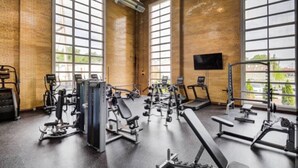 Un gimnasio con varios equipos de ejercicio, amplias ventanas y un televisor de pantalla plana en la pared.