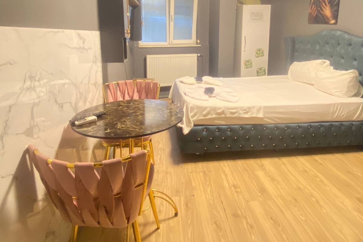 Ein Schlafzimmer mit einem Bett, einem runden Tisch mit Stühlen, einem Heizkörper, einem Fenster und einem an der Wand befestigten Fernseher.