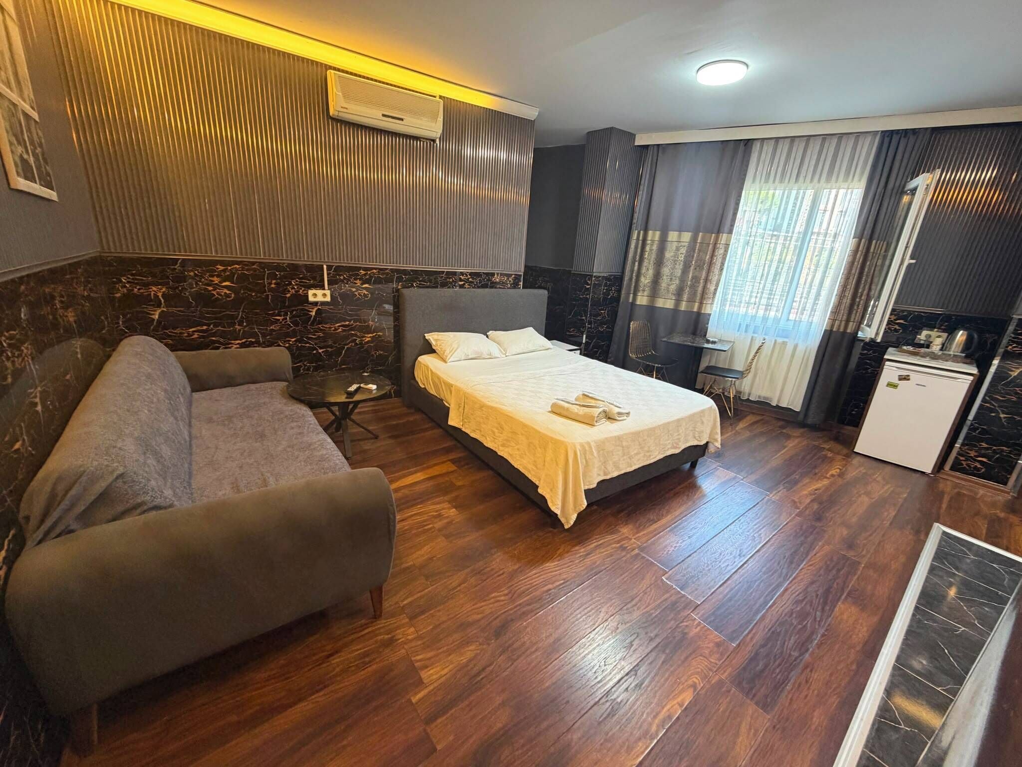 Habitación de hotel con cama, sofá, una mesita, kitchenette y ventana con cortinas.