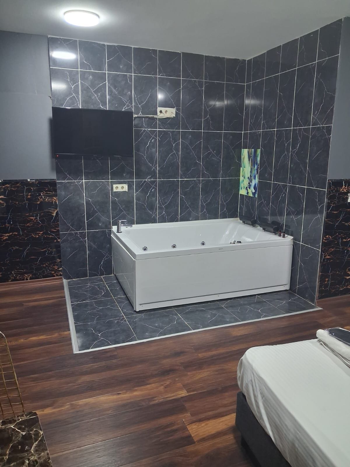 A modern bathroom with a freestanding bathtub, dark marble tiles, and a wooden floor.