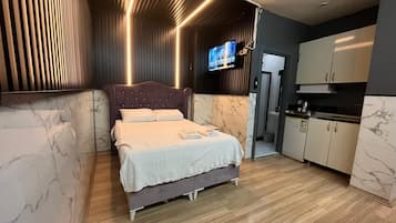 A modern bedroom with a large bed, a television, and a kitchenette.