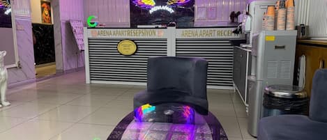Un área de recepción con un letrero de ala de neón, un mostrador de recepción, una mesa de vidrio con un posavasos y una estatua de un perro.