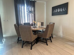 A dining area with a round table, four upholstered chairs, a chandelier, and a wall-mounted painting of the moon phases. - Spacious,brand new 4-bedroom house, sleeping upto 12 in Lodi with AC,heat &WiFi. (Lodi)