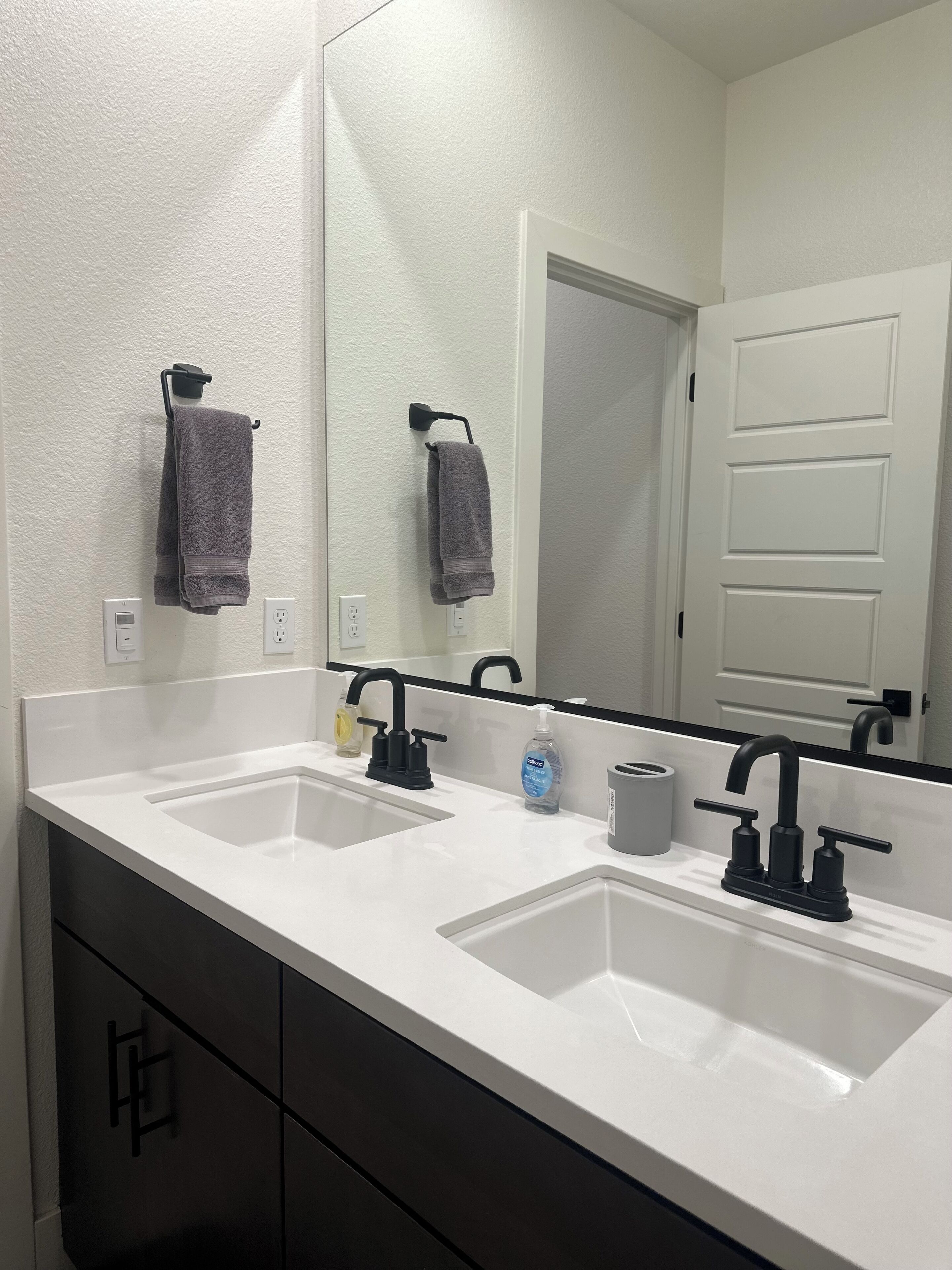 Une salle de bain avec deux lavabos, un grand miroir et une porte au fond.