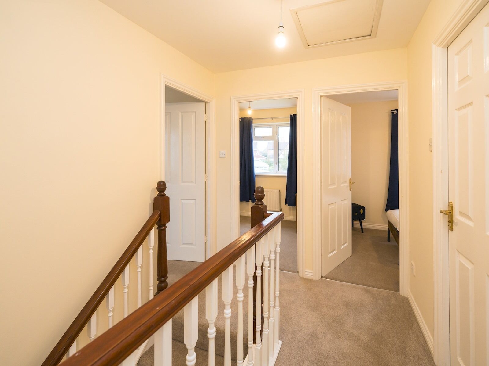 A hallway with a wooden staircase, white doors, and a view into a bedroom with a bed and a nightstand.