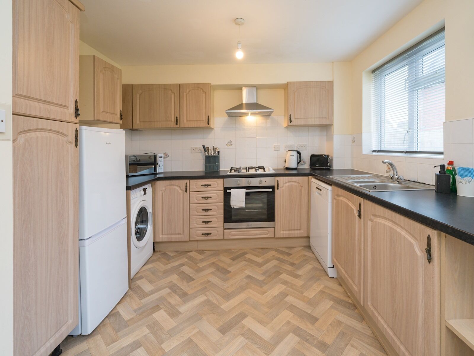 A modern kitchen with wooden cabinets, a built-in oven, a microwave, and a washing machine.