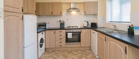 A modern kitchen with wooden cabinets, a built-in oven, a microwave, and a washing machine.
