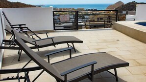 A rooftop terrace with lounge chairs and a pool, overlooking a coastal cityscape. - Sunset #105 Condominium - HD4 (Cabo San Lucas)