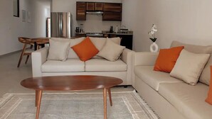 A modern living room with a sofa, coffee table, and kitchen in the background. - Sunset #105 Condominium - HD4 (Cabo San Lucas)