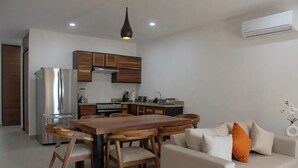 A modern kitchen with wooden cabinets, a stainless steel refrigerator, and a dining area with a wooden table and chairs. - Sunset #105 Condominium - HD4 (Cabo San Lucas)