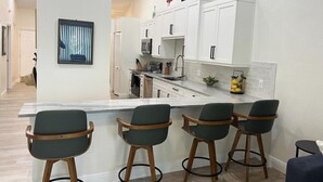 A modern kitchen with white cabinets, a central island with bar stools, and a view of the living area. - 2BR at Sandpiper Cove – Pool, Bay, Beachwalk (Englewood)