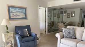 A living room with a blue armchair, a white sofa, a wooden coffee table, and a painting on the wall. - La Coquina 2BR – Beachfront w/ Pool & Views (Englewood)