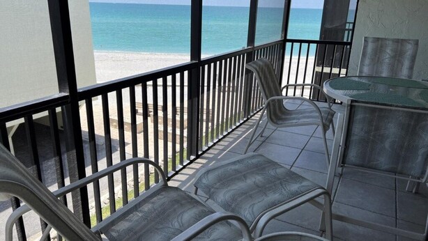 A balcony with metal chairs and a table, overlooking a beach. - La Coquina 2BR – Beachfront w/ Pool & Views (Englewood)