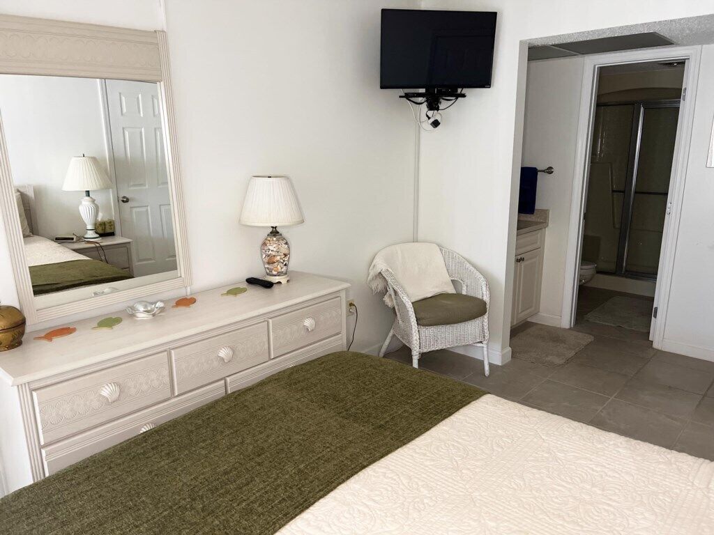 Un dormitorio con cama, cómoda, silla y televisor montado en la pared.