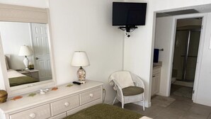 A bedroom with a bed, dresser, chair, and a TV mounted on the wall. - La Coquina 2BR – Beachfront w/ Pool & Views (Englewood)