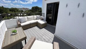 Un balcon avec un canapé en osier, une petite table agrémentée d’une plante et une porte-fenêtre coulissante.