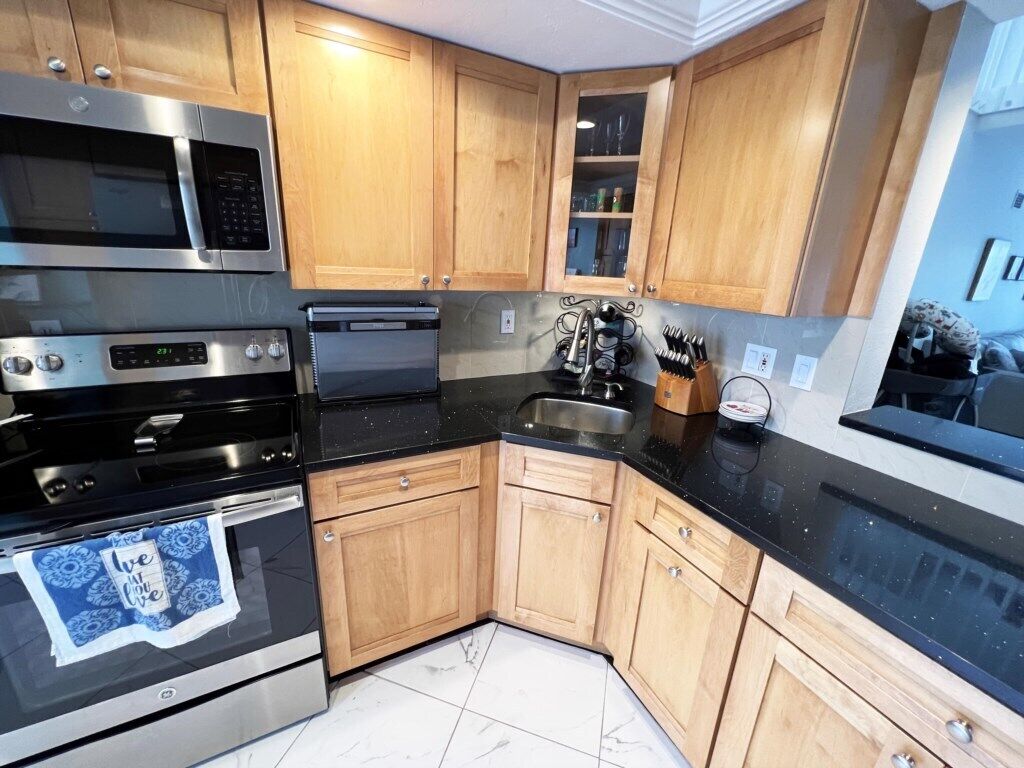 A kitchen with wooden cabinets, a black countertop, stainless steel appliances, and a tiled floor.