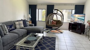 Una sala de estar con un sofá gris, una silla colgante, una mesa de centro y un televisor sobre un mueble.