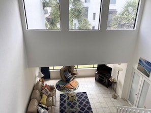 Una sala de estar con un sofá, una mesa de centro y un televisor. Tres ventanas proporcionan luz natural.