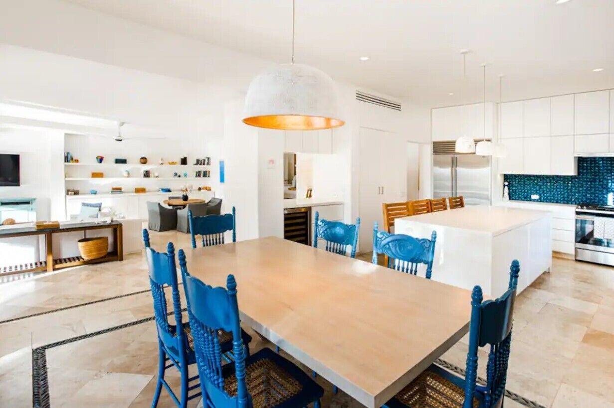 Een moderne keuken met witte kasten, een centraal eiland en blauwe stoelen.