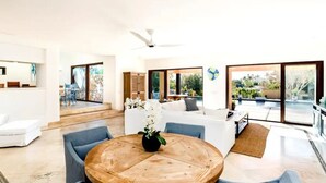 A spacious living area with a round wooden table, blue sofas, and a large sliding glass door leading to a balcony. - 4BD Residence in San José del Cabo (San José del Cabo)