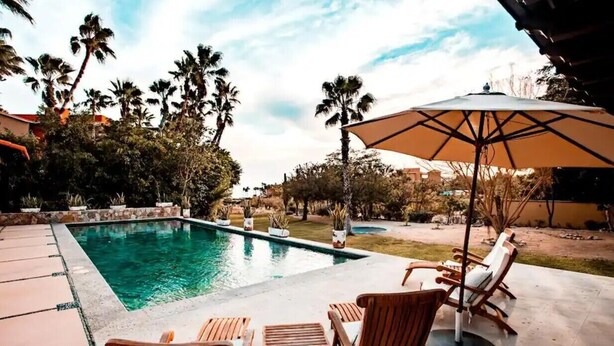 A swimming pool with lounge chairs and an umbrella, surrounded by palm trees and a garden. - 4BD Residence in San José del Cabo (San José del Cabo)