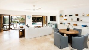 A spacious living area with a large white sofa, a round wooden table with chairs, and a TV mounted on the wall. - 4BD Residence in San José del Cabo (San José del Cabo)