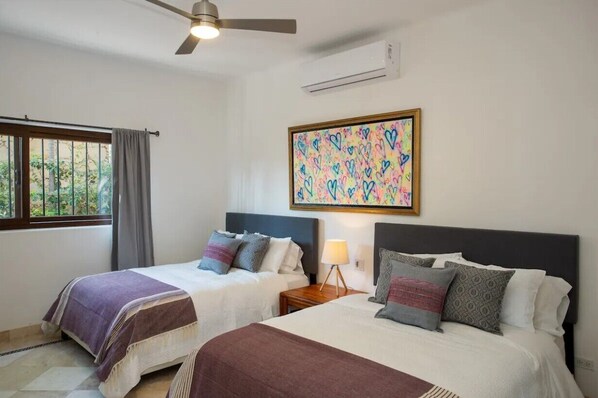 Quarto de hotel com duas camas, um ventilador de teto, ar condicionado e uma janela com cortinas.