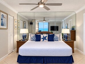 Ein Schlafzimmer mit einem großen Bett, zwei Nachttischen, einem Deckenventilator und Blick aufs Meer.
